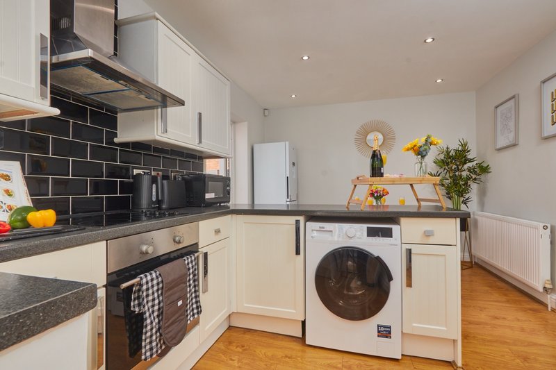 Modern kitchen with cream cabinets, black subway tile backsplash, white washing machine, and wooden flooring