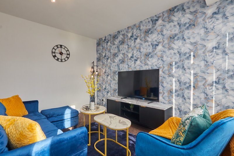Modern living room with blue sofas, patterned wallpaper, TV, and yellow accent pillows