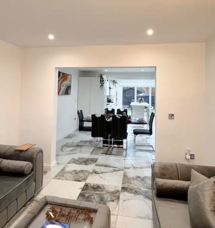 Open-plan living and dining area with marble-effect flooring, grey upholstered seating, and dining table visible through open doorway