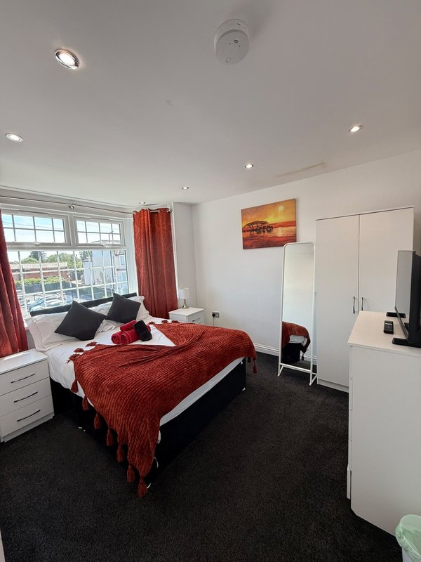 Bright bedroom with double bed, red bedding, white wardrobe, and large windows with red curtains