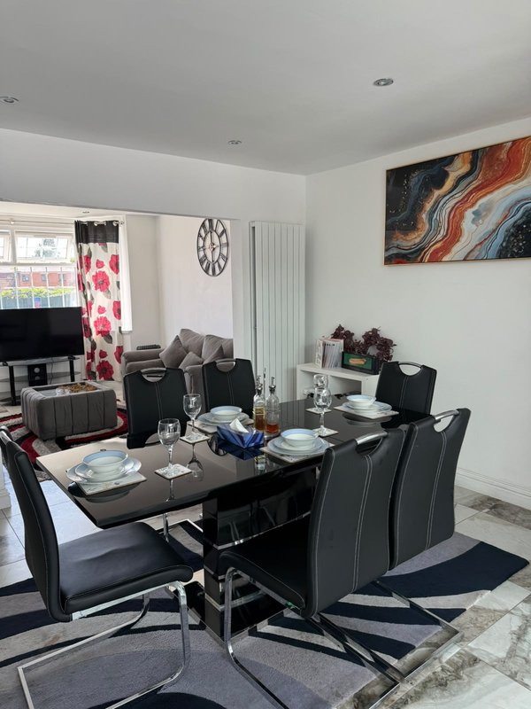 Modern dining room with black table, grey chairs, artwork and kitchen visible beyond