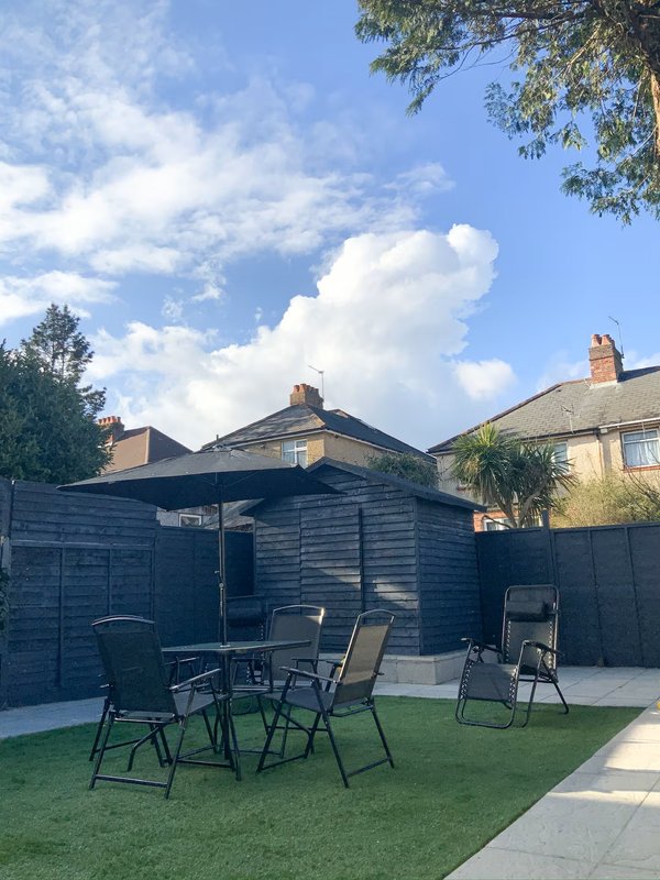Garden patio area with seating, black shed, lawn and surrounding residential buildings
