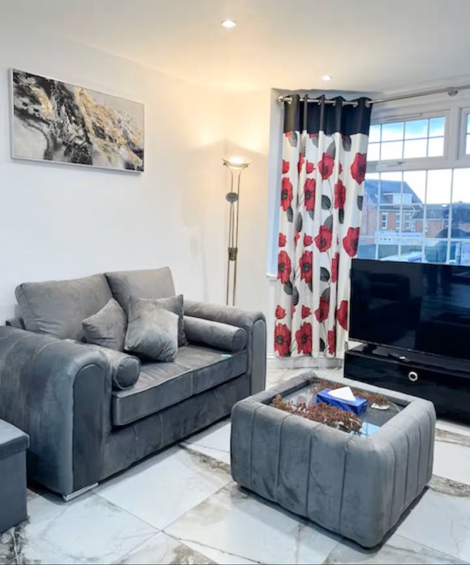 Modern living room with grey sofa, red patterned curtains, TV, and floor lamp