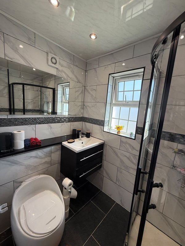 Modern bathroom with black vanity, white toilet, tiled walls, mirror and shower enclosure