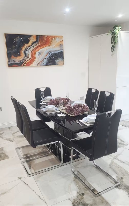 Modern dining room with black glass table, six black chairs, abstract wall art, and marble flooring