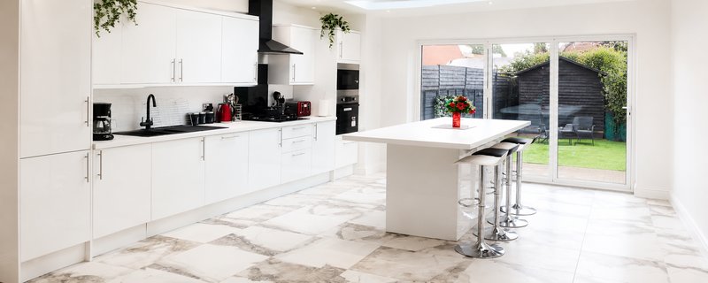 Modern kitchen with white cabinetry, marble flooring, island seating, and garden view
