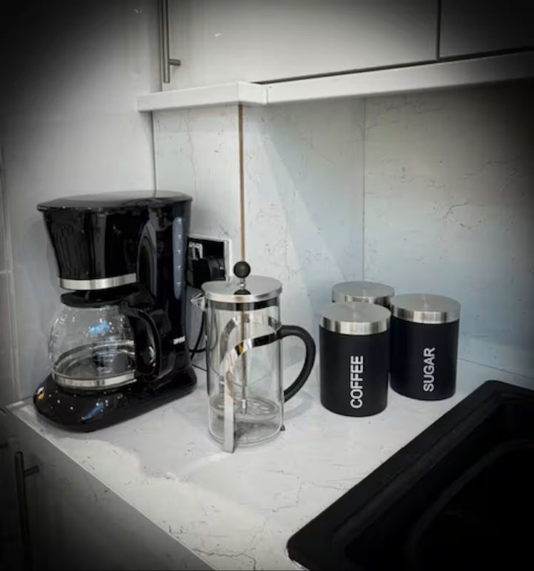 Kitchen counter with black coffee maker, glass carafe, French press, and branded mugs