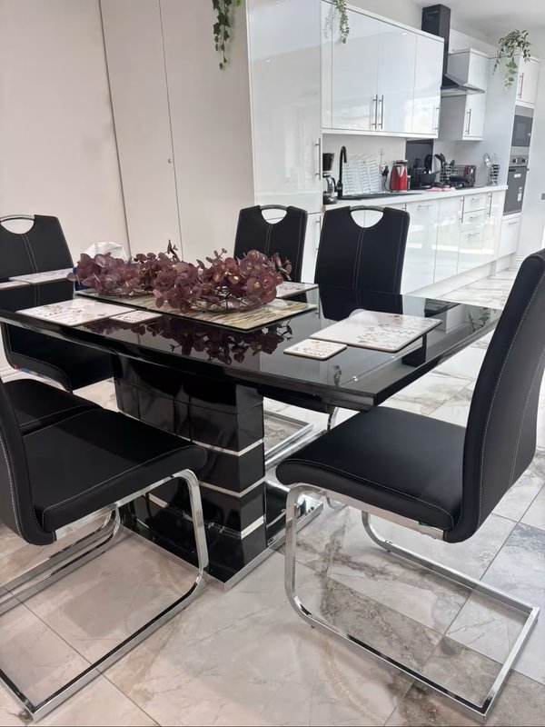 Modern dining room with black glass table, black chairs, and open-plan kitchen visible in background