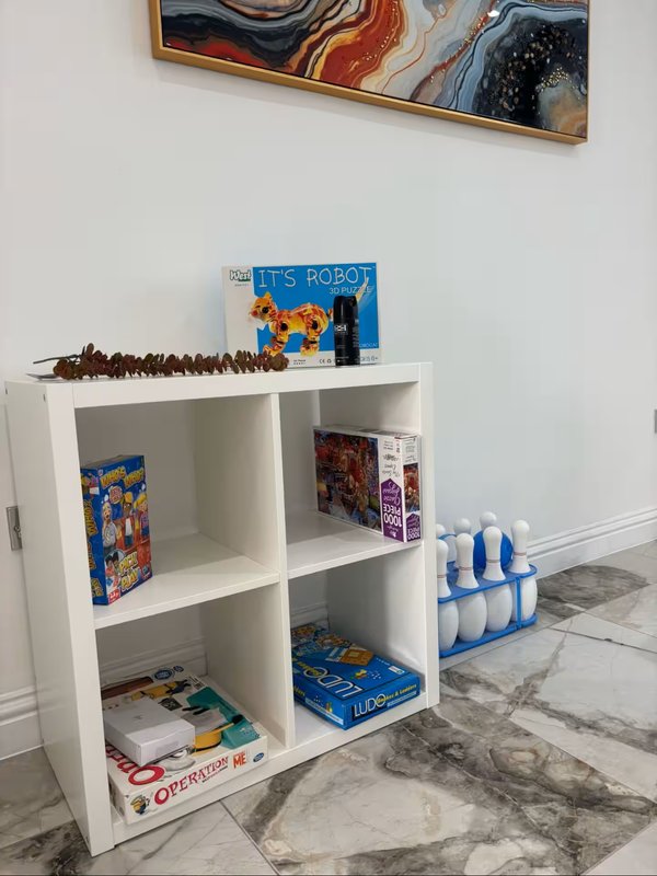 White shelving unit with board games, books, decorative items and blue bottles on marble floor