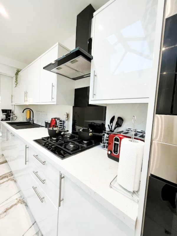 Modern kitchen with white cabinetry, black gas hob, stainless steel extractor hood and fridge