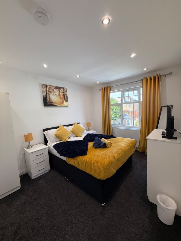 Bright bedroom with double bed, yellow bedding, gold curtains, and window overlooking street