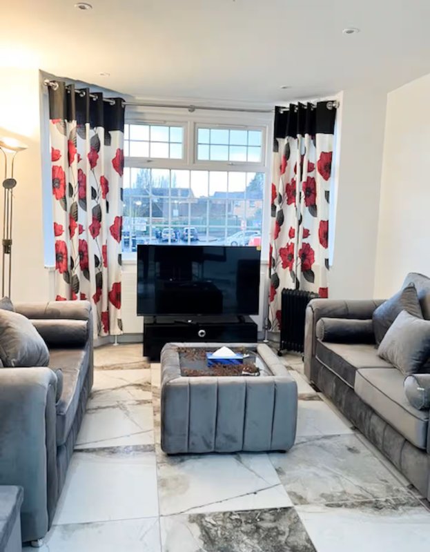 Modern living room with grey sofas, marble flooring, large windows and red patterned curtains