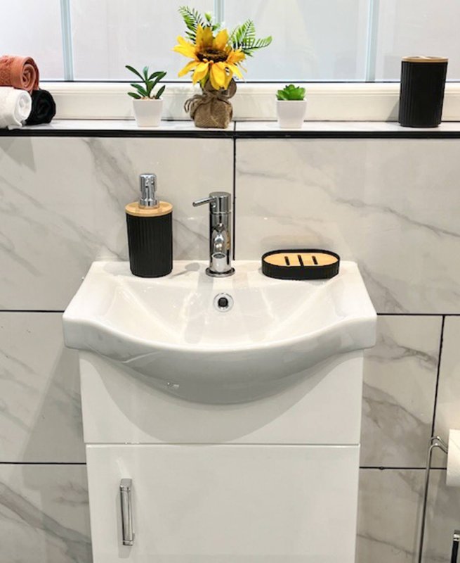 Modern bathroom sink with white vanity, marble splashback, and decorative items on shelf