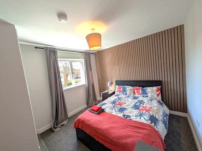 Bedroom with double bed, floral bedding, red throw, window with grey curtains, and corrugated accent wall