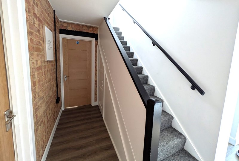 Hallway with brick wall, wooden door, staircase with gray carpet and black handrail