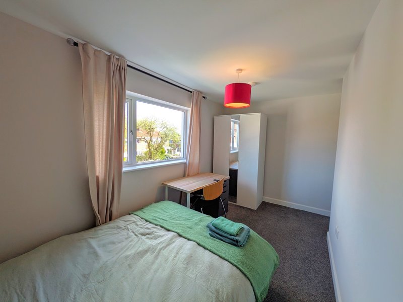 Bedroom with single bed, green bedding, desk, wardrobe, and window with curtains