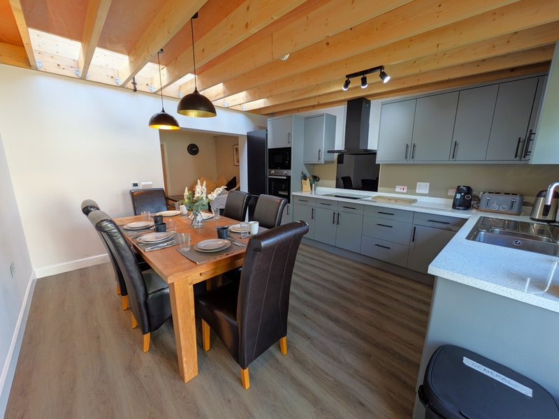 Open-plan kitchen and dining area with wooden table, grey cabinetry, and exposed beam ceiling