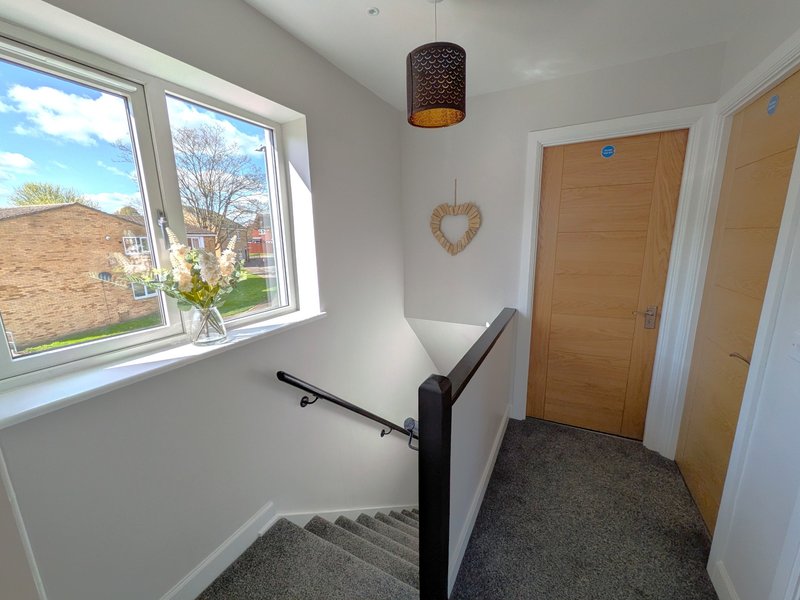 Bright stairwell landing with wooden doors, pendant light, window view and decorative heart