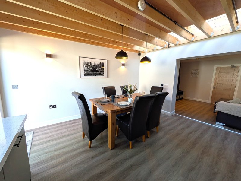 Open-plan living and dining area with wooden table, black chairs, pendant lights, and wood ceiling.