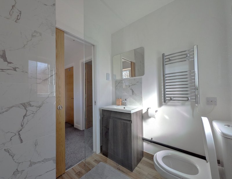 Modern bathroom with marble-effect tiles, dark vanity, toilet, heated towel rail and shower enclosure