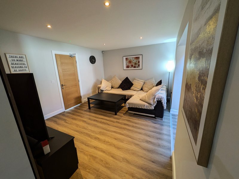 Spacious living room with cream sectional sofa, wooden flooring, wall art and recessed lighting