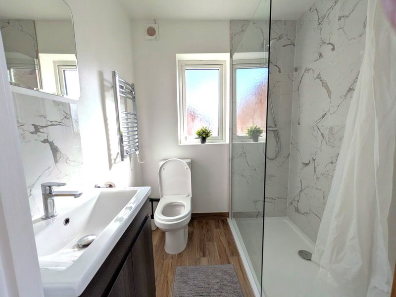 Modern bathroom with white sink, toilet, glass shower enclosure and marble-effect tiles