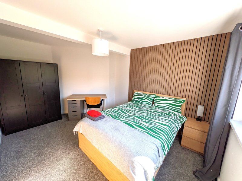Bedroom with double bed, striped curtains, desk, wardrobe and wooden bedside table