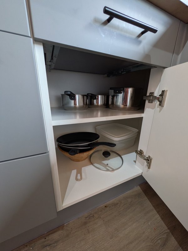 Open kitchen cabinet showing cookware, pans, lids and stainless steel containers on shelves