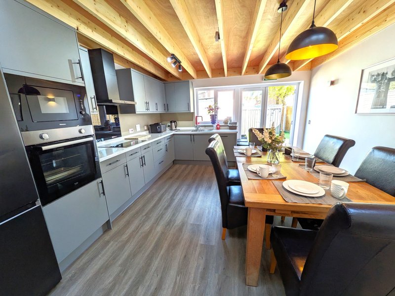 Modern kitchen-diner with wooden beams, white cabinetry, dining table and chairs