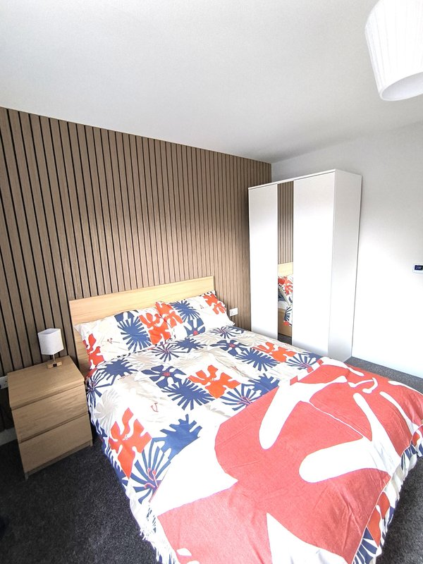Modern bedroom with double bed, floral bedding, wooden headboard and white wardrobe