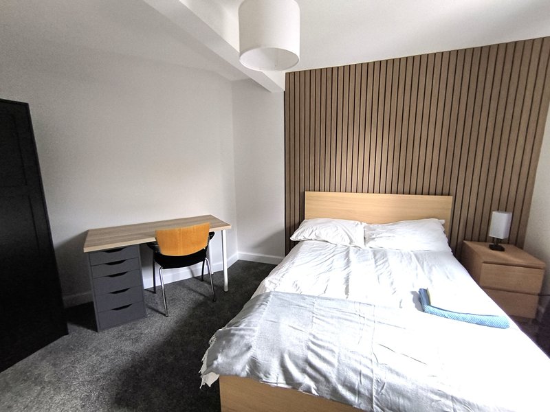 Modern bedroom with double bed, wooden headboard, desk, chair and bedside table