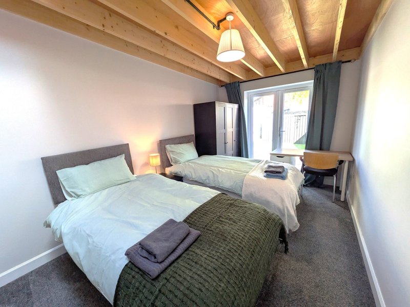 Bright bedroom with two single beds, wooden beams, bedside lamps and glass doors