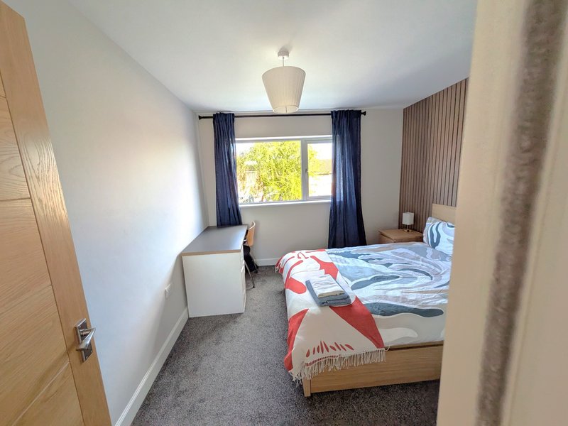 Bright bedroom with double bed, desk, chair, window with blue curtains and pendant ceiling light
