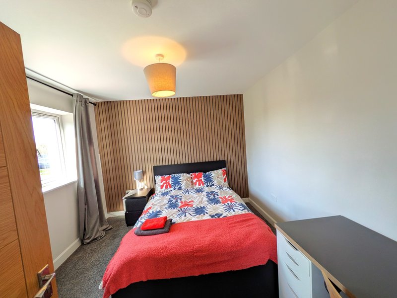 Bedroom with single bed, patterned duvet, red blanket, wooden headboard and ceiling light