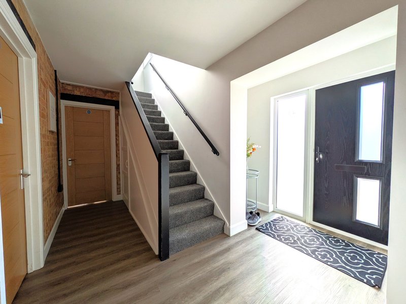 Bright entrance hallway with stairs, wooden doors, and dark glass front doors with sidelight windows