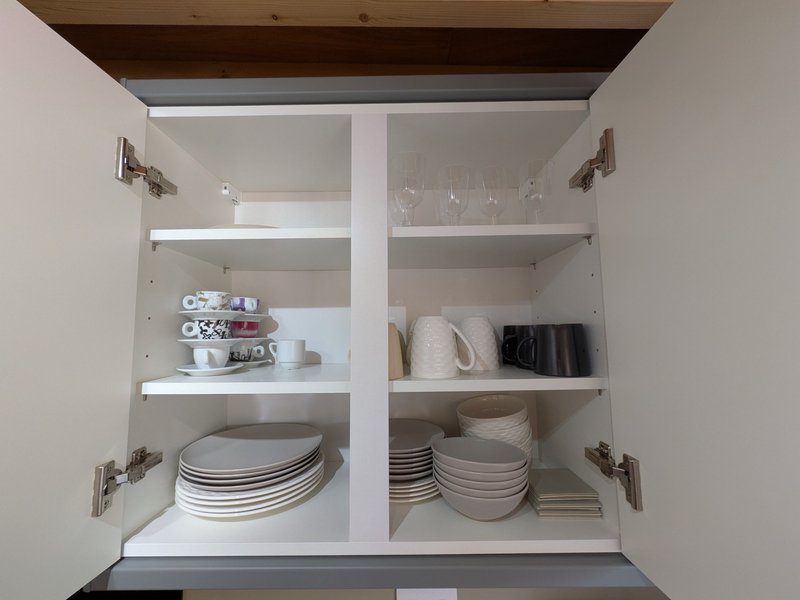 Open kitchen cabinet with shelves displaying stacked plates, bowls, cups and kitchenware