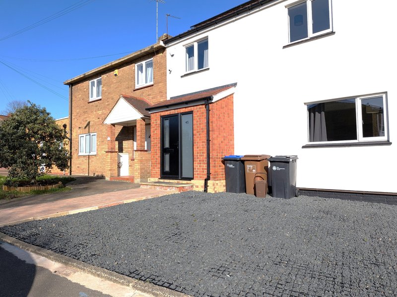 Modern brick house with driveway, front entrance, and parked bins on gravel