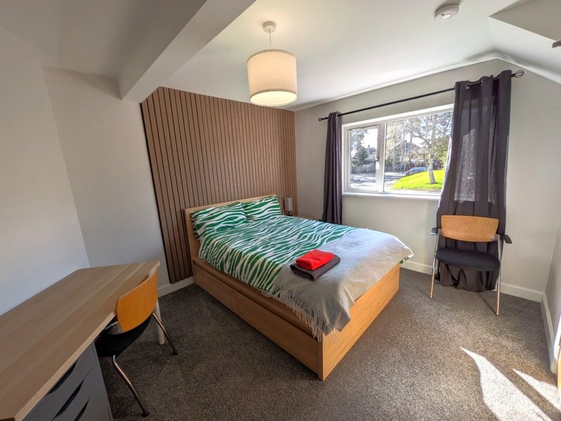 Modern bedroom with wooden bed frame, striped bedding, desk, and large window with view