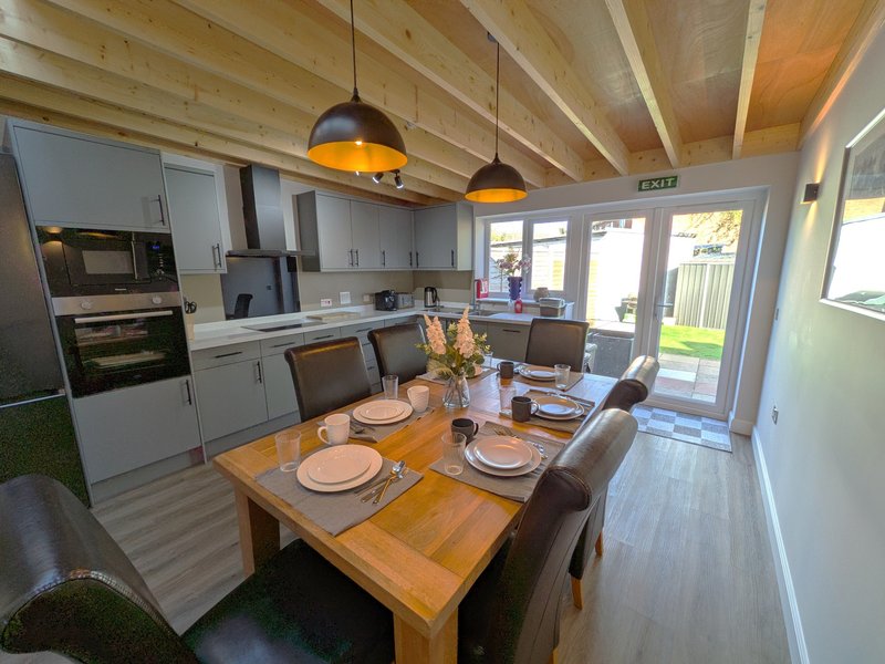 Modern kitchen-diner with wooden table, white cabinetry, pendant lights and garden view