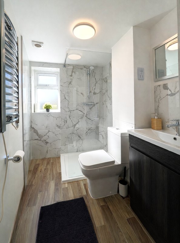 Modern bathroom with marble shower enclosure, black vanity, toilet, and wooden floor
