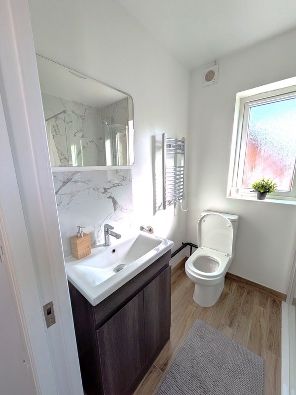 Modern bathroom with white sink vanity, mirror, toilet, wooden flooring and window