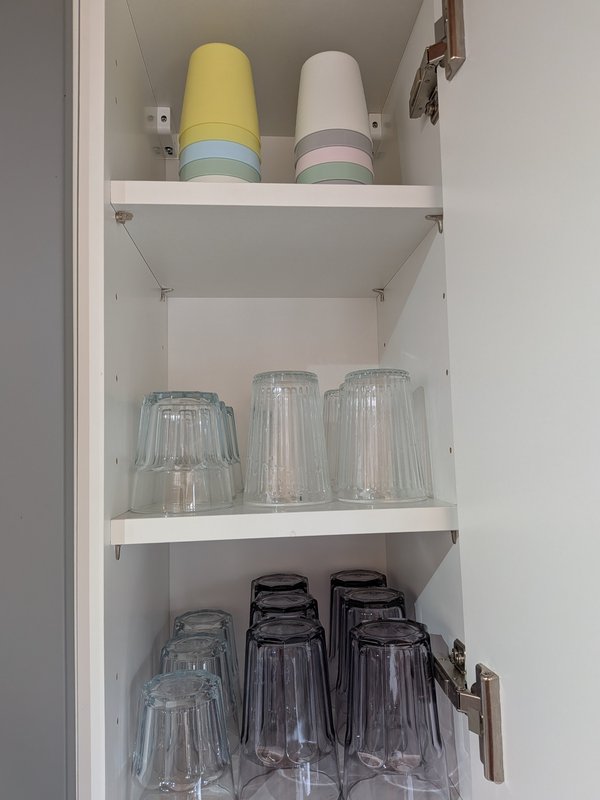 Open kitchen cabinet with storage containers, glasses, and dishware organized on white shelves