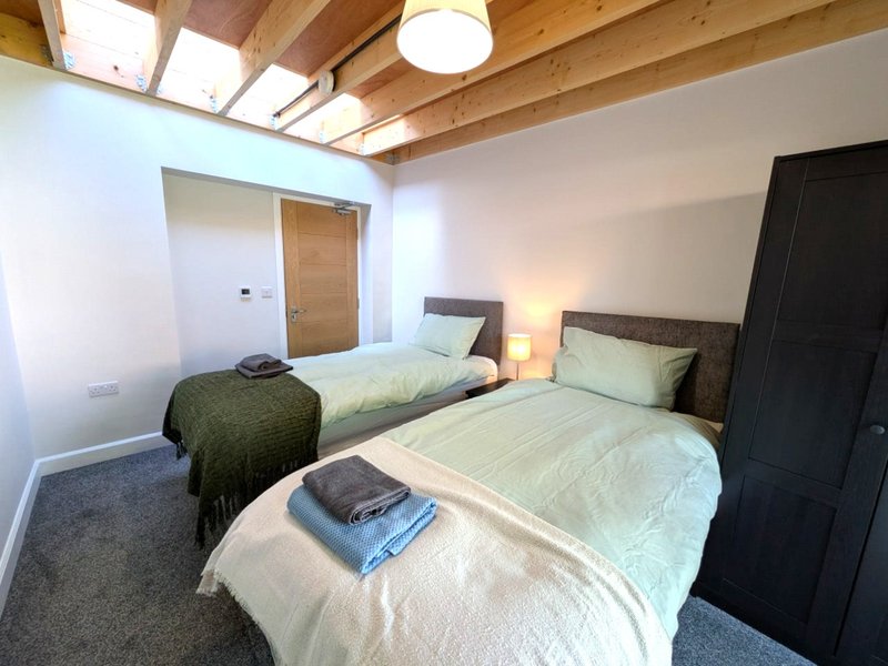 Bright bedroom with two single beds, wooden ceiling beams, skylight and bedside lamps