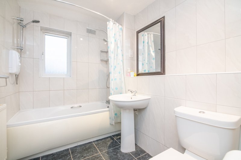Clean modern bathroom with bathtub, pedestal sink, toilet, and window