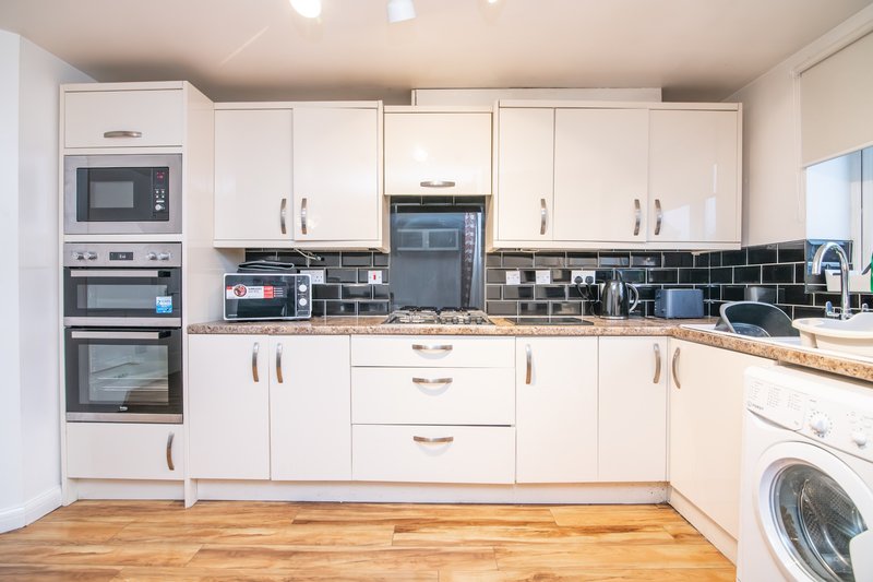 Modern kitchen with white cabinetry, black tile backsplash, stainless steel appliances and wooden flooring