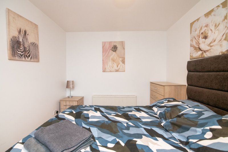 Bedroom with double bed, geometric bedding, wooden headboard, and framed wall art