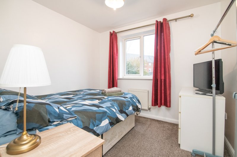 Bedroom with single bed, blue patterned duvet, bedside lamp, red curtains and wall-mounted TV