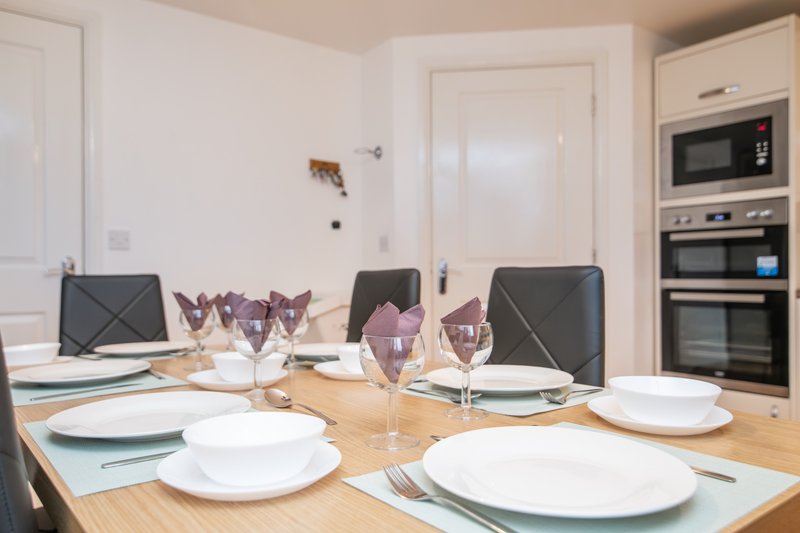 Modern kitchen and dining area with wooden table set for dining, black chairs, and integrated appliances