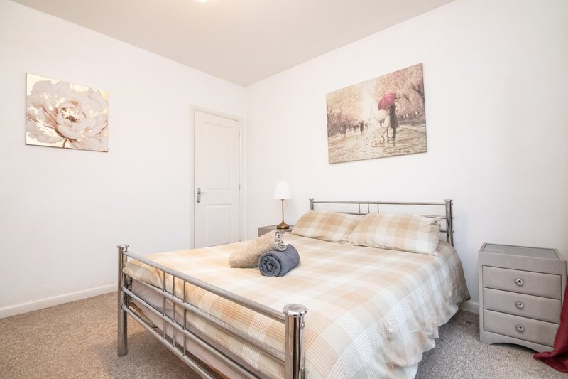 Bright bedroom with metal-frame bed, beige checkered bedding, wooden nightstand, and wall art