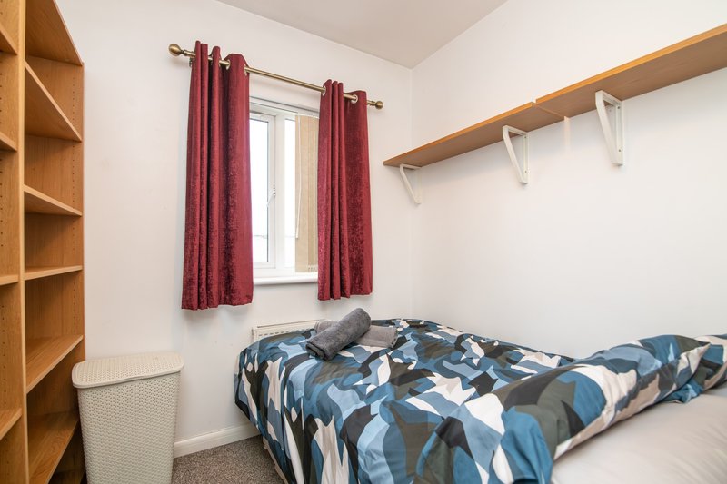 Small bedroom with single bed, blue patterned duvet, wooden shelving and burgundy curtains